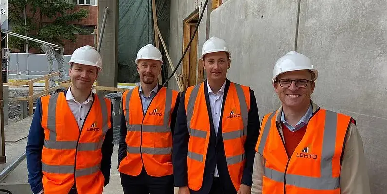 Vier M&auml;nner in orangenen Westen und mit Helmen stehen auf einer Baustelle