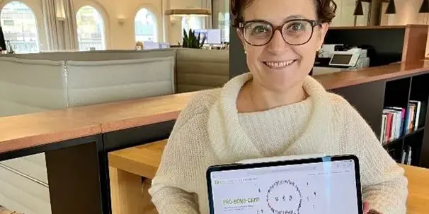 Irene steht im B&uuml;ro, h&auml;lt ein Ipad hoch und l&auml;chelt in die Kamera