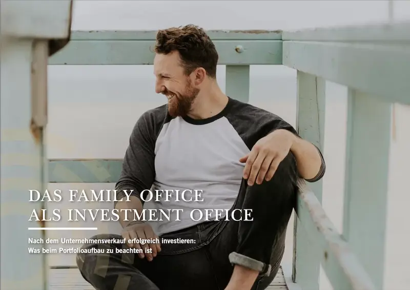 Ein Mann sitzt auf einem Holzgerüst und guckt freudig zur Seite