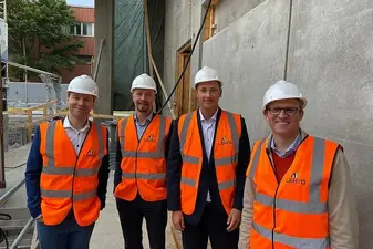 Vier Männer in orangenen Westen und mit Helmen stehen auf einer Baustelle