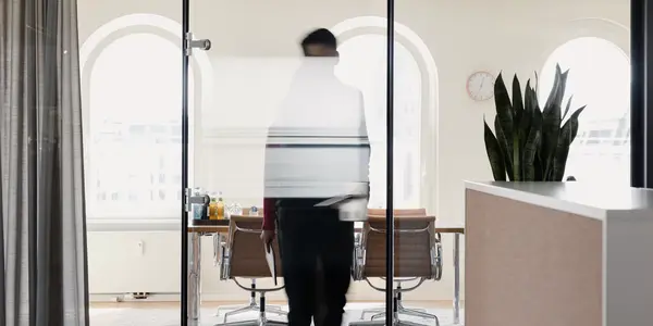 A Man standing behind a glass wall in the office. He himself ist noch clearly identifiable