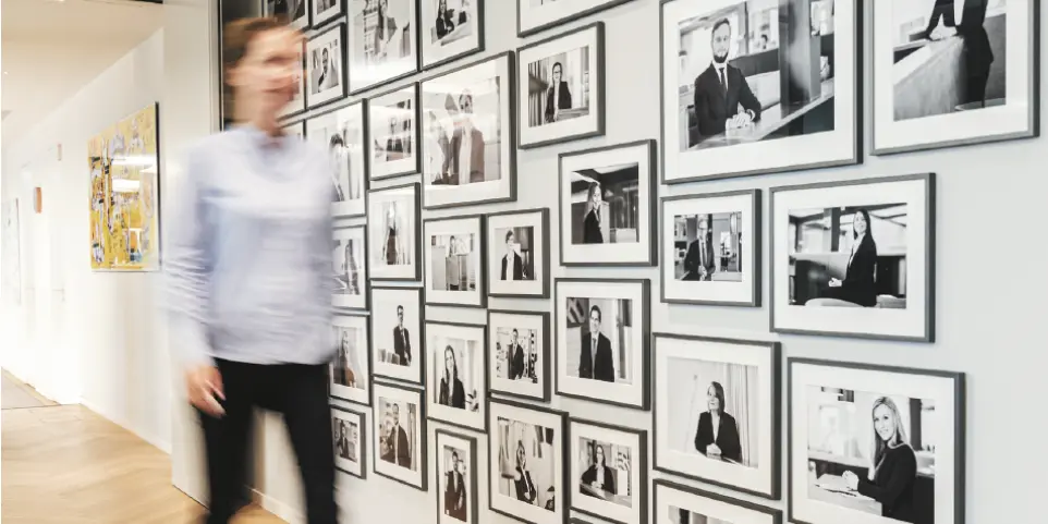 Eine Frau geht an einer Bilderwand vorbei. Die Aufnahme ist verschwischt