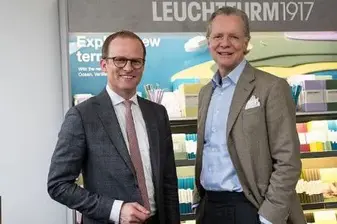 Patrick Maurenbrecher und Axel Stürken stehen vor einem Schreibwarenregal und gucken in die Kamera