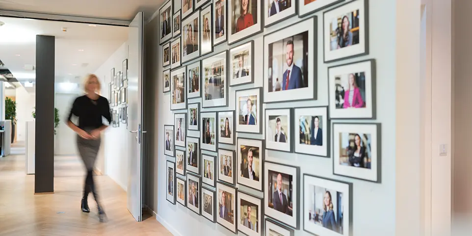 Eine Frau geht an einer Wand mit Mitarbeiterfotos vorbei