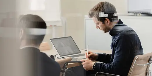 Two men are working in a conference room at laptops